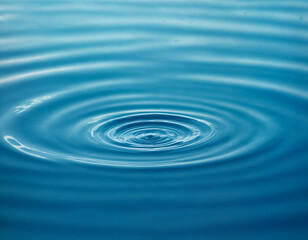 A single water droplet creates concentric ripples on a serene blue surface, capturing the elegance of motion and the tranquility of nature. This image symbolizes simplicity, purity, and the ripple eff