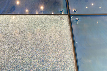 Shattered facade glass panel with visible cracks, need safe replacement. Multilayered safety glass remains intact, preventing shards from falling. Glass technology, damage control, glass replacement