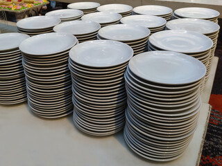 The image shows several stacks of white ceramic plates arranged neatly on a table. Each stack...