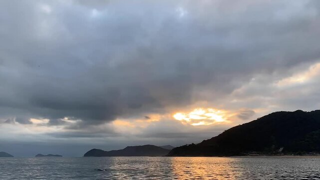 Time-lapse fim de tarde com c&eacute;u nublado e os raios do sol passando pelas nuvens e tamb&eacute;m refletindo no mar.