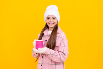 happy kid in hat and mittens with coffee or tea cup on yellow background, warm tea