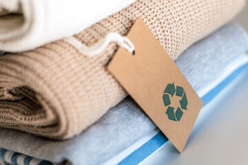 Knitted warm clothes neatly folded heap with craft tag recycling material circle arrow closeup