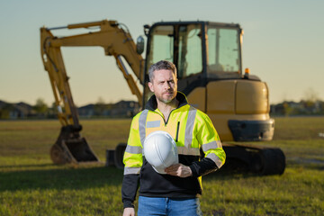 Naklejka premium Worker at construction site. Builder in hardhat. Construction man with helmet. Worker at construction with helmet. Industry worker at construction building. Builder at site building with excavator.
