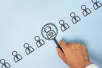 A hand holding a magnifying glass focusing on a robot icon among a row of human icons, representing...