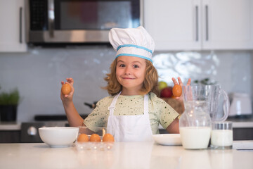 Kid chef cook with eggs at kitchen. Funny little kid chef cook wearing uniform cook cap and apron...