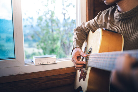 Close up of a man hands playing guitar for worship God at the window, christian background, devotional concept.