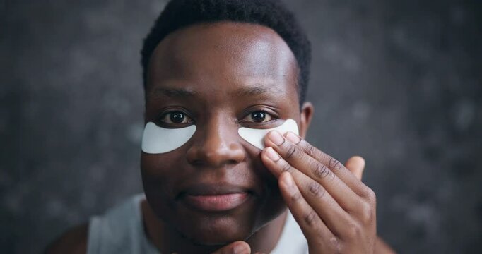Face, black man and happy with eye patches for skincare, hygiene and glow in dark background. Male person, facial mask and smile or satisfied with cosmetics product for self care and grooming