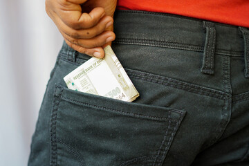 A black Indian man is putting a few Indian rupees notes into his back pocket. He is removing money from his pocket and holding it.