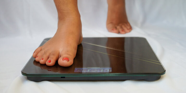 A young woman barefoot and stepping on floor scales. Woman feet standing weighing scales, slimming. Weight loss scales measure weight. Health and wellness.