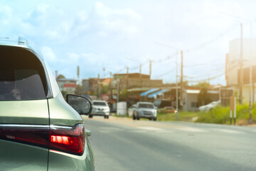 Generated ImageRear side of car green pastel colors with turn on brake light. Driving on the aspahlt road with other cars opposits of road. Blurred background of small town under the sky.