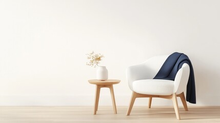 A cozy white chair with a navy throw and a small wooden table, adorned with a flower vase, set against a minimalist wall.