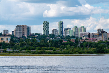 High rise residential buildings on the river bank against a cloudy sky.