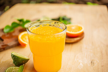 A glass of freshly squeezed orange juice on a wooden table surrounded by orange slices and orange leaves