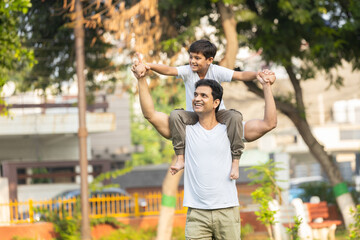 happy indian father giving son piggyback ride on his shoulders in park. Childhood and parenting...