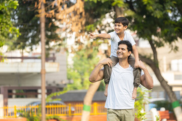 happy indian father giving son piggyback ride on his shoulders in park. Childhood and parenting...