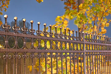Ornate iron fence with decorative spikes and circular patterns, set against a backdrop of autumn...