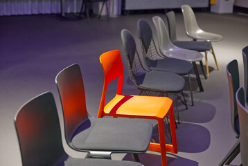 In a row of dark chairs, an orange-red chair stands as a special feature