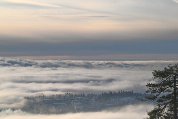 From the Holmenkollen in Oslo you have a sublime view of the fog over Oslo from the mountain and look from above at the clouds with sun above in the depths of winter with snow on roofs and Trees