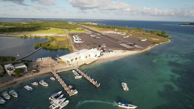 Small plane takes off from Los Roques airport on a sunny day with boats in the turquoise water below