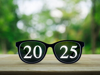 2025 white text with black eye glasses on wooden table over blur green tree in park, Business happy...