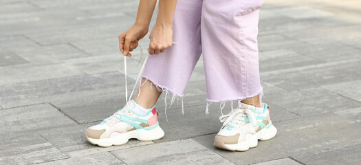Young woman in stylish sneakers tying shoe laces outdoors, closeup