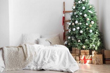 Interior of festive bedroom with comfortable bed and Christmas tree