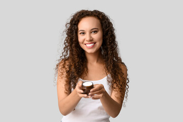 Naklejka premium Beautiful young African-American woman with jar of face cream on white background