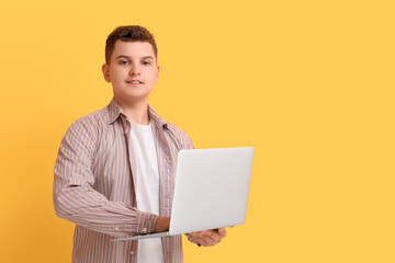 Teenage boy using modern laptop on yellow background