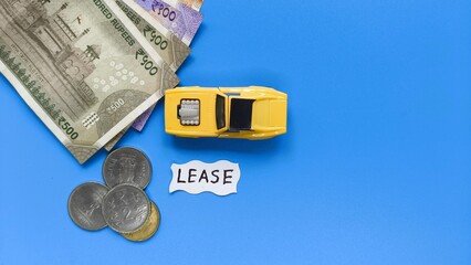 Car lease or rent creative concept. Toy car vehicle on blue table background near Indian rupee bank currency notes and coins with copy space. Car lease word or text written on white paper.