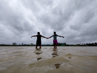 Silhouette of Two People Walking in Flooded Water Under Dramatic Cloudy Sky
