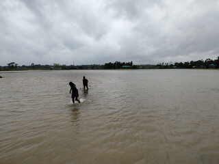 Silhouette of Two People Walking in Flooded Water Under Dramatic Cloudy Sky