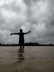 Silhouette of a Person Standing in Flooded Water Against a Dramatic Overcast Sky