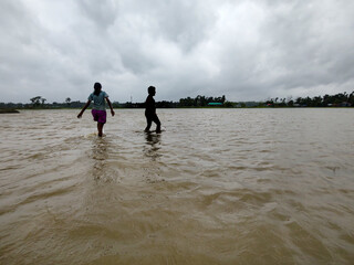 Silhouette of Two People Walking in Flooded Water Under Dramatic Cloudy Sky