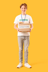 Young male volunteer with donations on yellow background