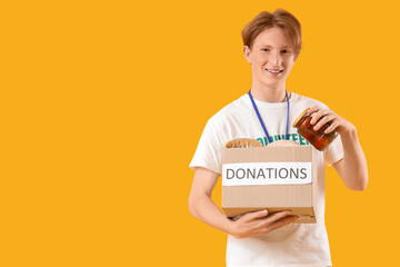 Young male volunteer with donations on yellow background