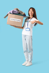 Young female volunteer with donations on blue background