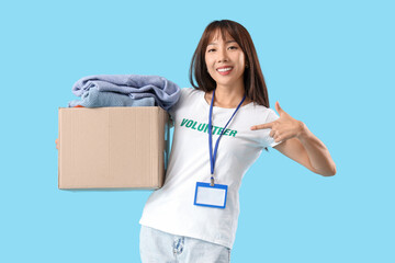 Young female volunteer with donations on blue background