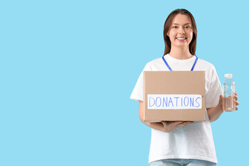 Young female volunteer with donations on blue background