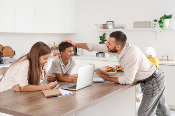 Cute little children with their father doing homework in kitchen at home