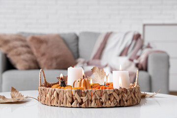 Wicker tray with glowing candles and autumn leaves on table in room