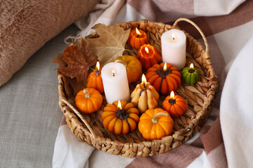 Wicker tray with glowing candles and autumn leaves on sofa in room