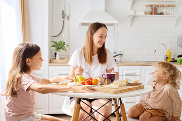 A mother shares a joyful breakfast with her two daughters at a sunny kitchen table, enjoying fresh fruits, pancakes, and laughter in a cozy atmosphere