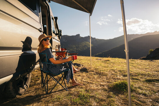 A woman relaxes by a camper van, enjoying a remote retreat with picturesque mountain scenery