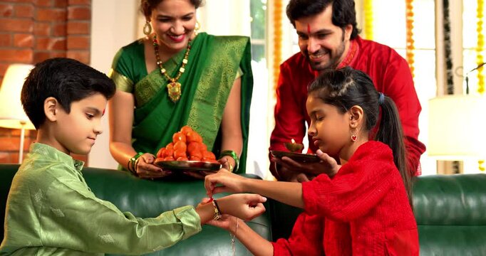 Rakshabandhan Festival - Closeup of Indian Family Celebrating with Daughter Tying Rakhi to Brother and Exchanging Gifts in Traditional Attire at Home