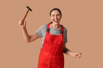 Young female construction worker with hammer on beige background. Woman in male profession concept