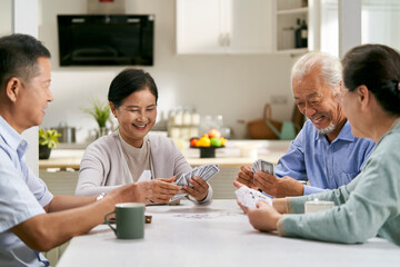 Obraz premium group of happy senior asian people two couples playing cards at home