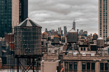 A cloudy New York City skyline featuring iconic rooftop water towers, historic architecture, and modern high-rises, capturing urban contrast