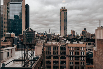 A cloudy New York City skyline featuring iconic rooftop water towers, historic architecture, and modern high-rises, capturing urban contrast