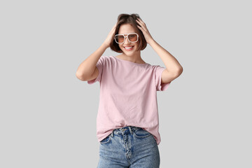 Young woman in blank t-shirt and sunglasses on grey background