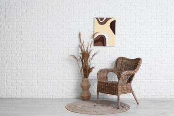 Armchair, pampas grass in vase and picture on white brick wall in room